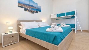 A hotel room with a bed, a bedside table with a lamp, a bunk bed, and a wall-mounted artwork. - Vrbo Property (Napoli)
