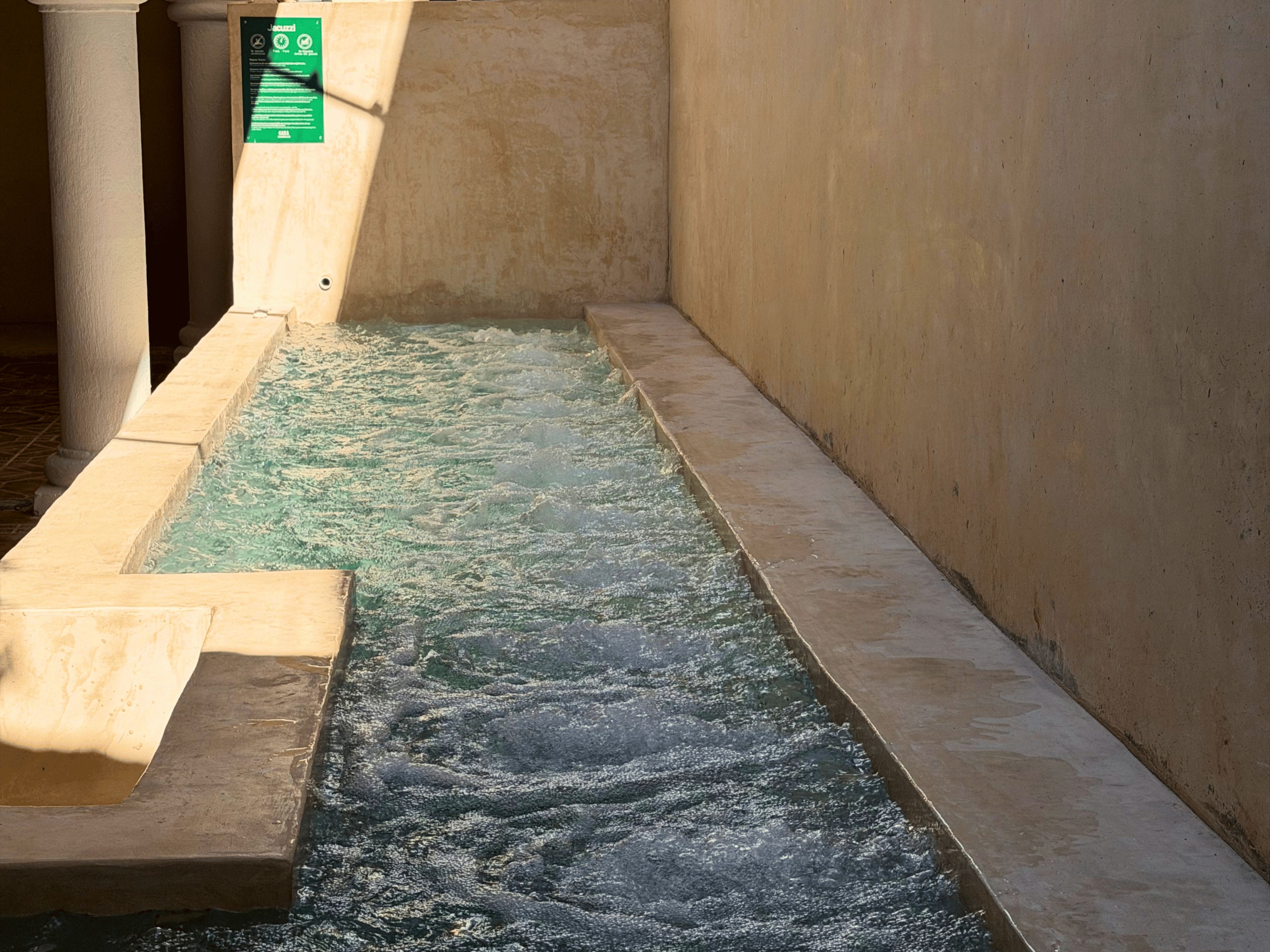 A water feature with a flowing stream in a confined space, bordered by walls and a column.