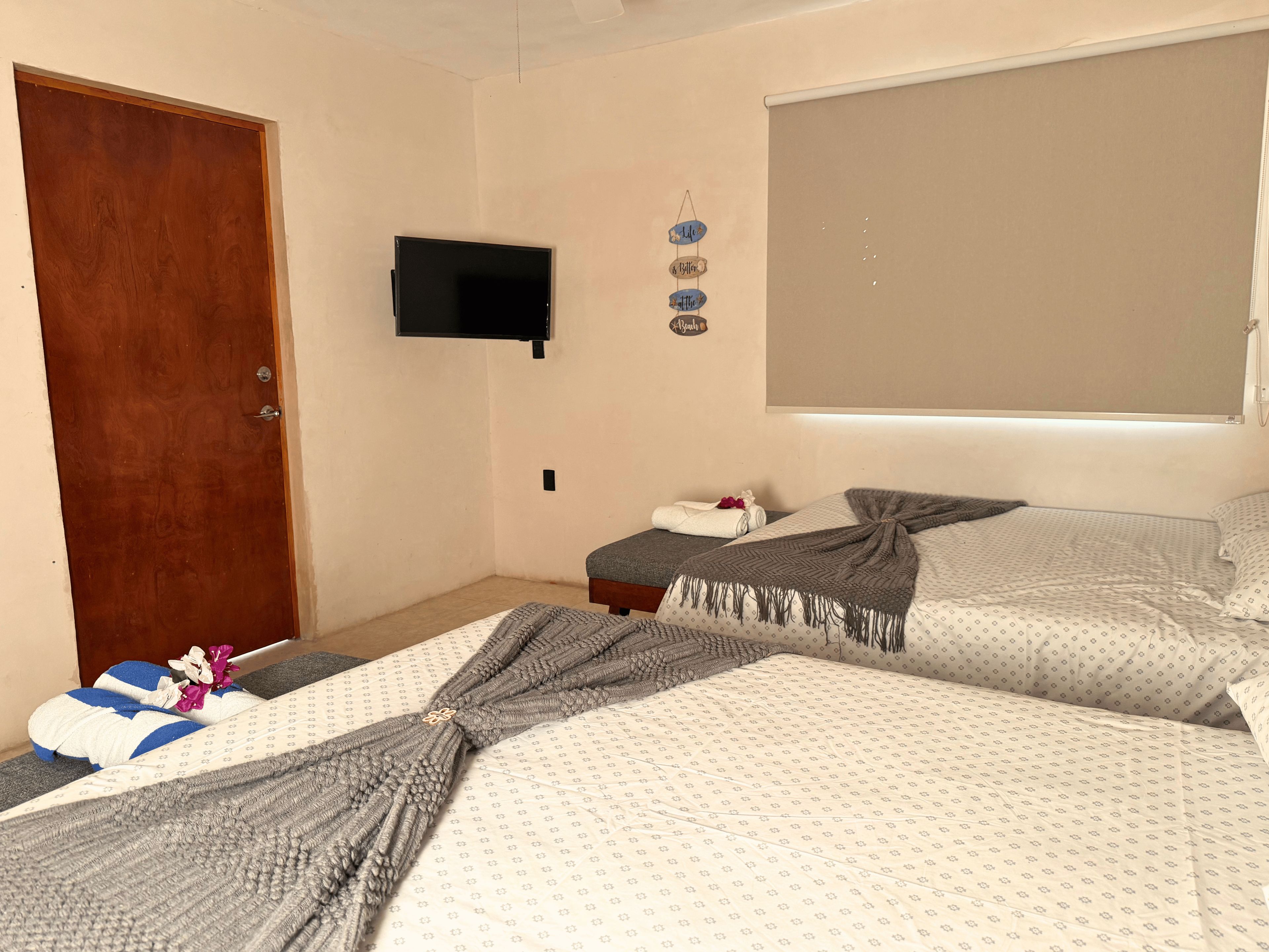 A bedroom with two beds, a television on the wall, and a wooden door.