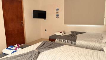 A bedroom with two beds, a television on the wall, and a wooden door.
