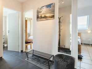 A hallway with a bench, a wicker ottoman, a coat rack, and a painting on the wall. - Holiday Home With 2 Bedrooms (St. Peter-Ording)