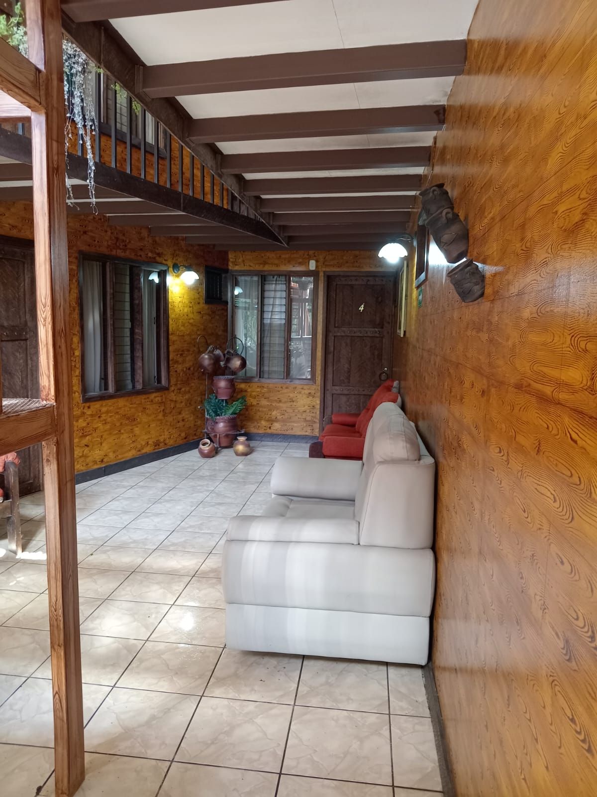 A room with a wooden ceiling, a sofa, a red chair, and a window with curtains.
