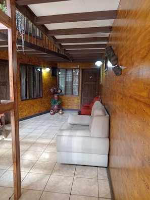 Una habitación con techo de madera, un sofá, una silla roja y una ventana con cortinas.