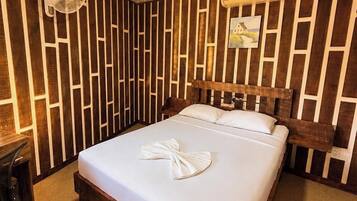 Habitación de hotel con cama de madera, escritorio, ventilador de pared y aire acondicionado.