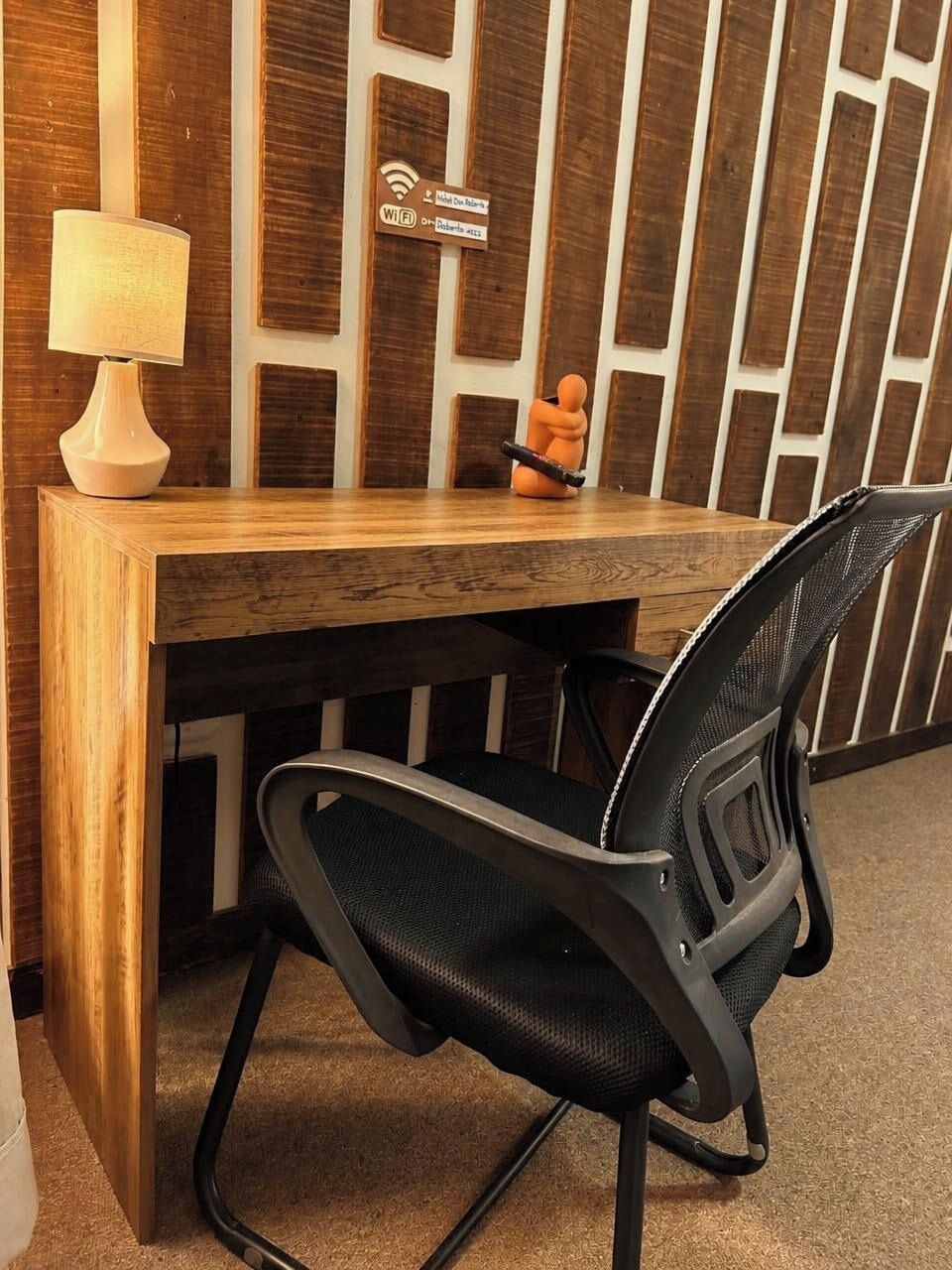 Un escritorio de madera con una lámpara, una silla y un cartel que indica acceso a Wi-Fi.