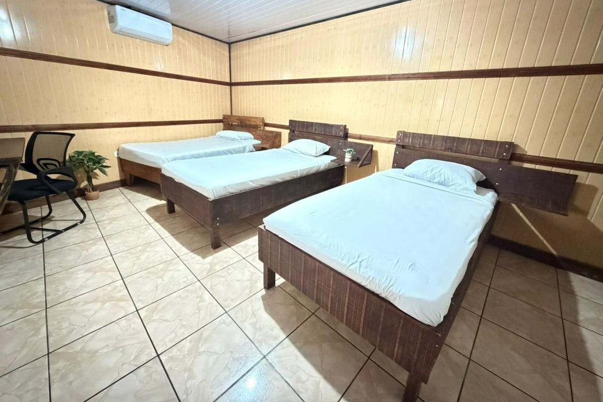 A room with two beds, a chair, a desk, and an air conditioning unit.