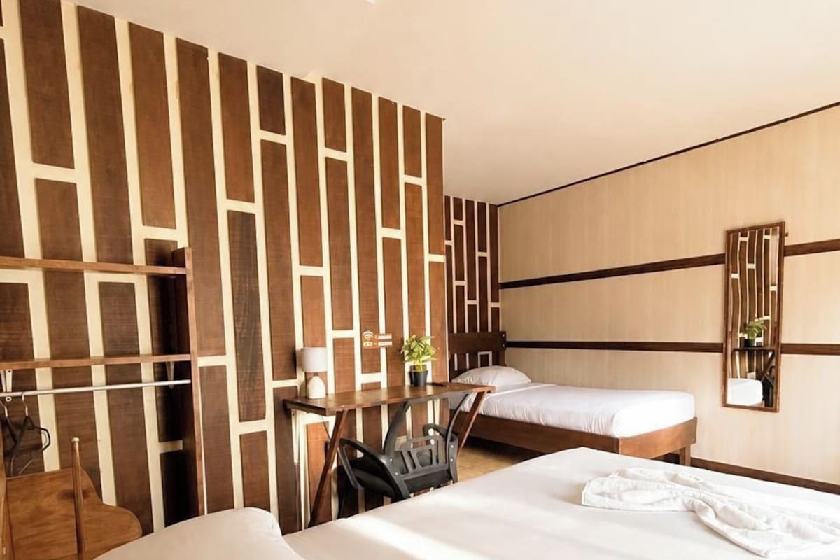 A hotel room with a large bed, a desk, and a chair. There is a wooden panel wall and a mirror on the wall.