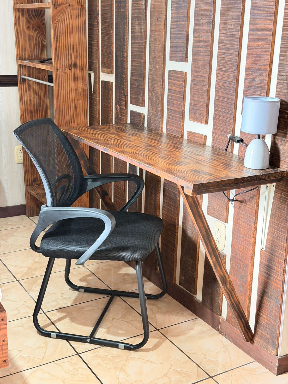 A wooden desk with a chair, a lamp, and a power outlet.
