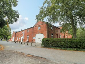 Ein rot backsteins Gebäude mit mehreren Fenstern und Türen, umgeben von Bäumen und einer Hecke.