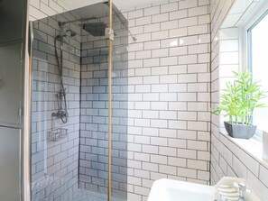 Een moderne badkamer met een douchecabine van glas, witte betegelde wanden en een plant in een pot bij het raam.