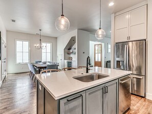 A modern kitchen with a central island, stainless steel appliances, pendant lighting, and a dining area with a view. - Beautiful 4 Bed 2.5 Bath Home in Wheeler District (Oklahoma City)