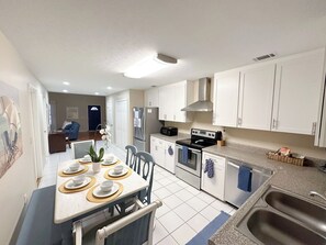 A modern kitchen with white cabinets, a dining table set with plates, and a built-in oven. - Private Retreat Home on Quiet North End of Tybee Island (Tybee Island)