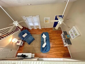 A room with a staircase, two blue sofas, a white table, and a ceiling fan. - Private Retreat Home on Quiet North End of Tybee Island (Tybee Island)