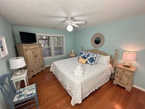 A bedroom with a bed, a ceiling fan, a television on a cabinet, a lamp, and a chair. - Private Retreat Home on Quiet North End of Tybee Island (Tybee Island)