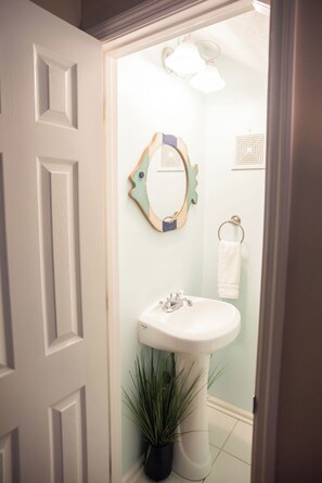 A bathroom with a white door, a sink, a mirror, and a potted plant. - Private Retreat Home on Quiet North End of Tybee Island (Tybee Island)