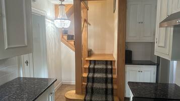 Une cuisine avec un escalier en bois, un lustre et un poêle noir.