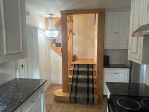 A kitchen with a wooden staircase, a chandelier, and a black stove.
