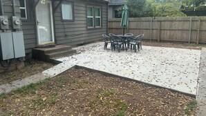 En lukket gårdhave med en beton terrasse, et træhegn og et bord med stole.
