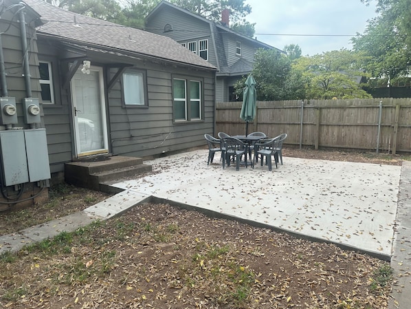 A residential backyard with a concrete patio, a wooden fence, and a table with chairs.