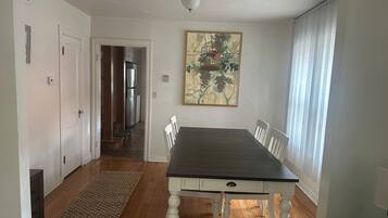 A dining area with a table, chairs, a rug, and a painting on the wall.