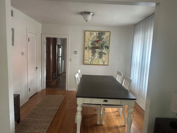 A dining area with a table, chairs, a rug, and a painting on the wall.