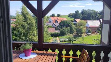 Eine Holzterrasse mit Tisch und Stühlen, einem Blumentopf und Blick auf eine ländliche Landschaft mit Häusern und viel Grün.