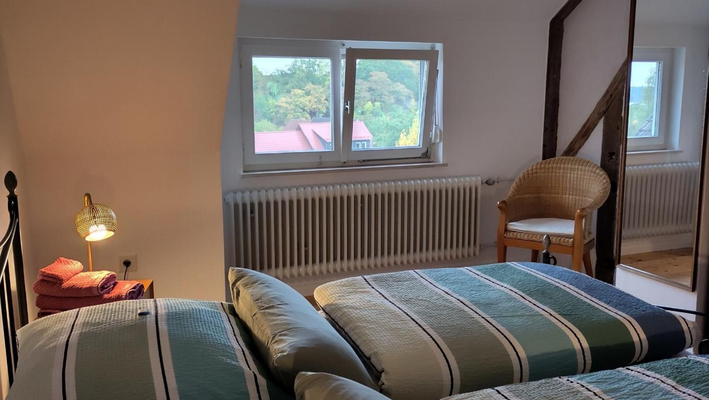 Ein Schlafzimmer mit Bett, Stuhl, Heizkörper und einem Fenster mit Blick auf Häuser.
