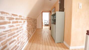 Ein schmaler Flur mit einer Backsteinwand und einer weißen Wand, der zu einem Schlafzimmer mit Bett und Kleiderschrank führt.