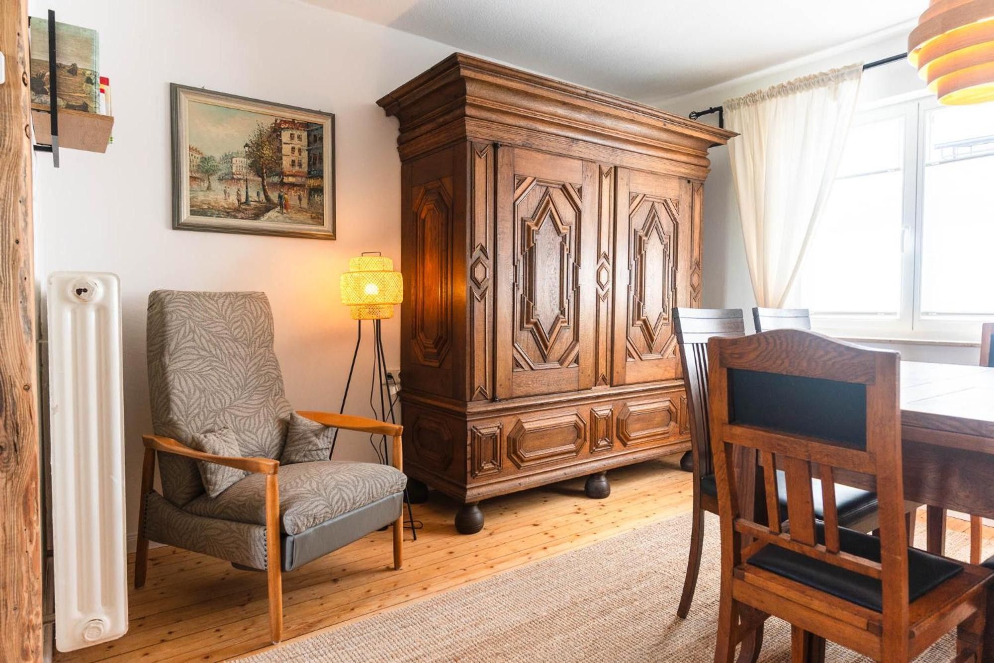 Una habitación con un armario de madera, una silla, una mesa y una lámpara de pie.