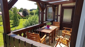 Ein Holzbalkon mit Tisch und Stühlen, mit Blick auf eine grüne Landschaft.