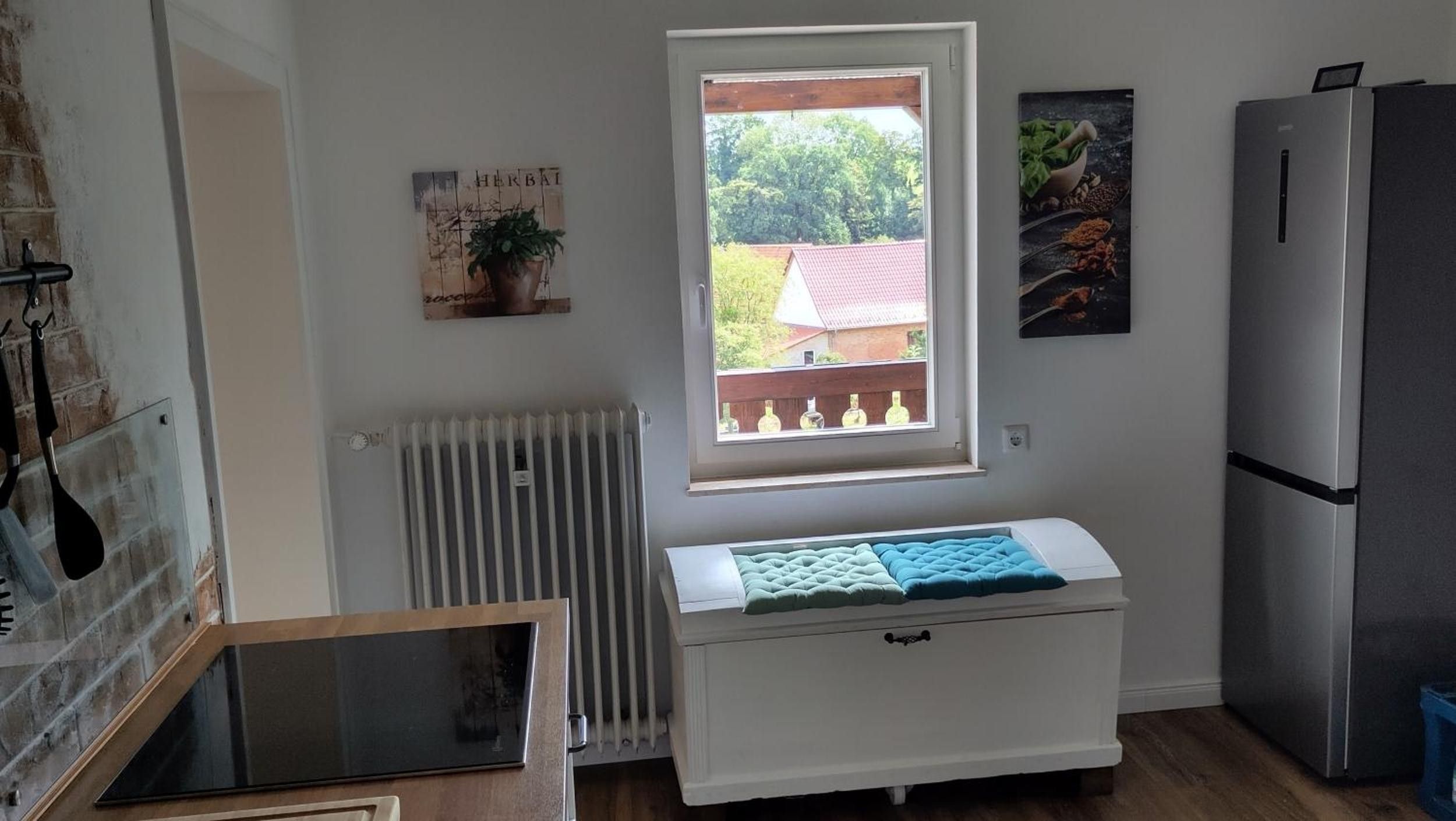 Eine Küche mit Fenster, Heizkörper, Kühlschrank und einer kleinen Bank mit Kissen.
