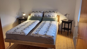 Ein Doppelbett mit einem gemusterten Überwurf, zwei Nachttische jeweils mit einer Lampe und ein Holzboden.