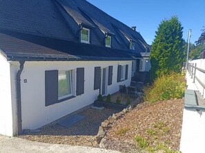 A white building with a dark roof, numbered 12, featuring multiple windows and a small outdoor seating area. - Holiday Apartment 706 (Winterberg)