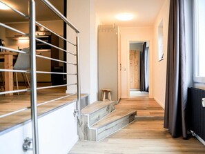 A hallway with a staircase leading to a room, a radiator, and a window with curtains. - Holiday Apartment 706 (Winterberg)