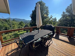 Eine Holzterrasse mit Tisch, Stühlen, Sonnenschirm und Grill.