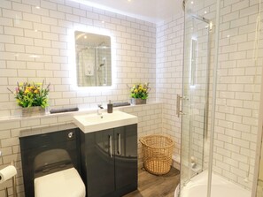 A modern bathroom with a glass shower enclosure, a black vanity with a sink, and two flower arrangements on the countertop. - No.31 Craigard Road (Callander)