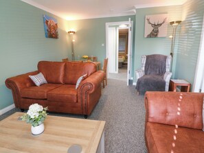 A living room with a brown sofa, a grey armchair, and a wooden coffee table with a white vase. - No.31 Craigard Road (Callander)