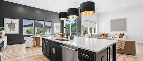 A modern kitchen with a large island, black cabinetry, stainless steel appliances, and pendant lighting.