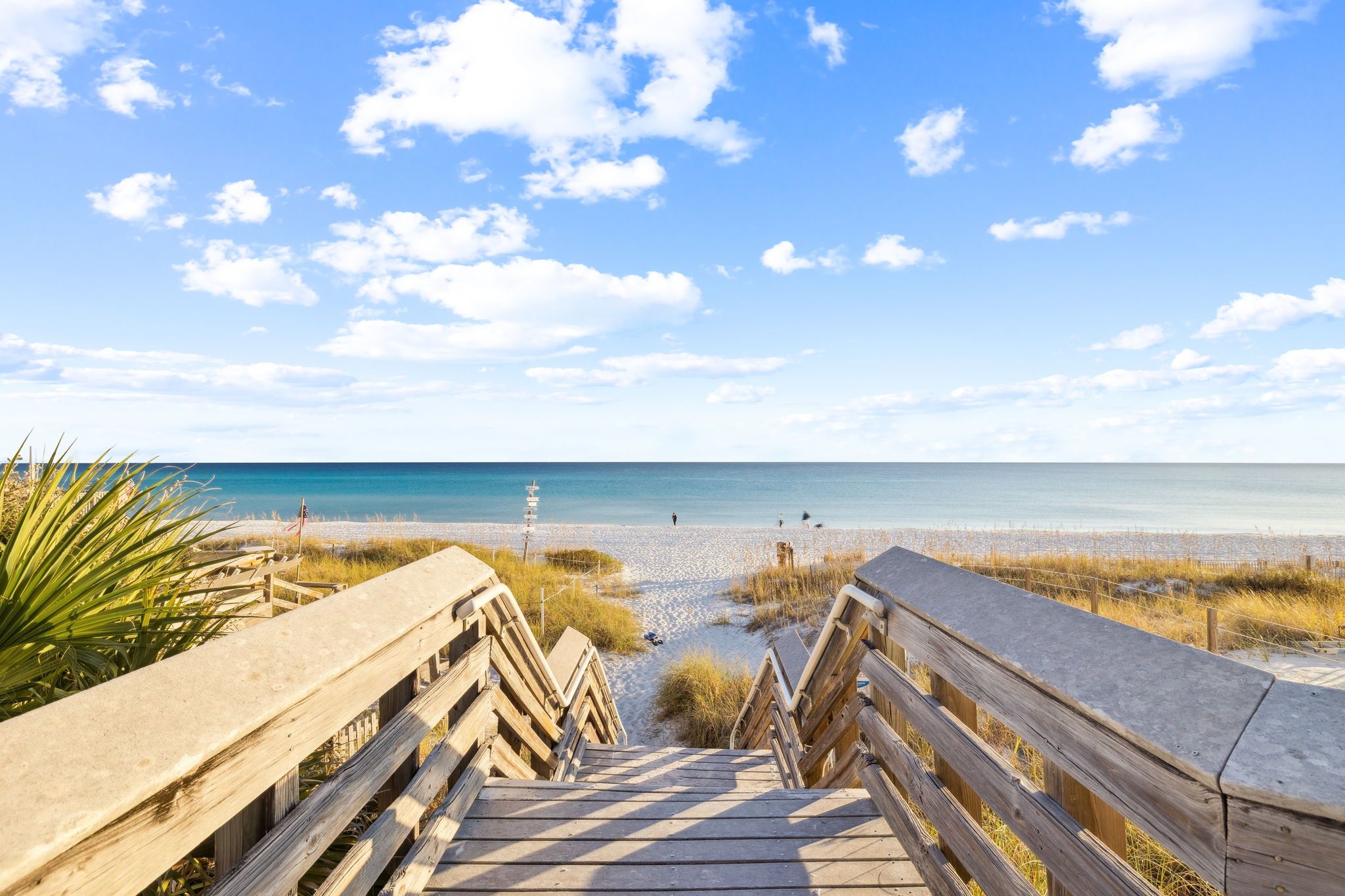 A wooden boardwalk leading to a beach with a clear sky and calm sea.