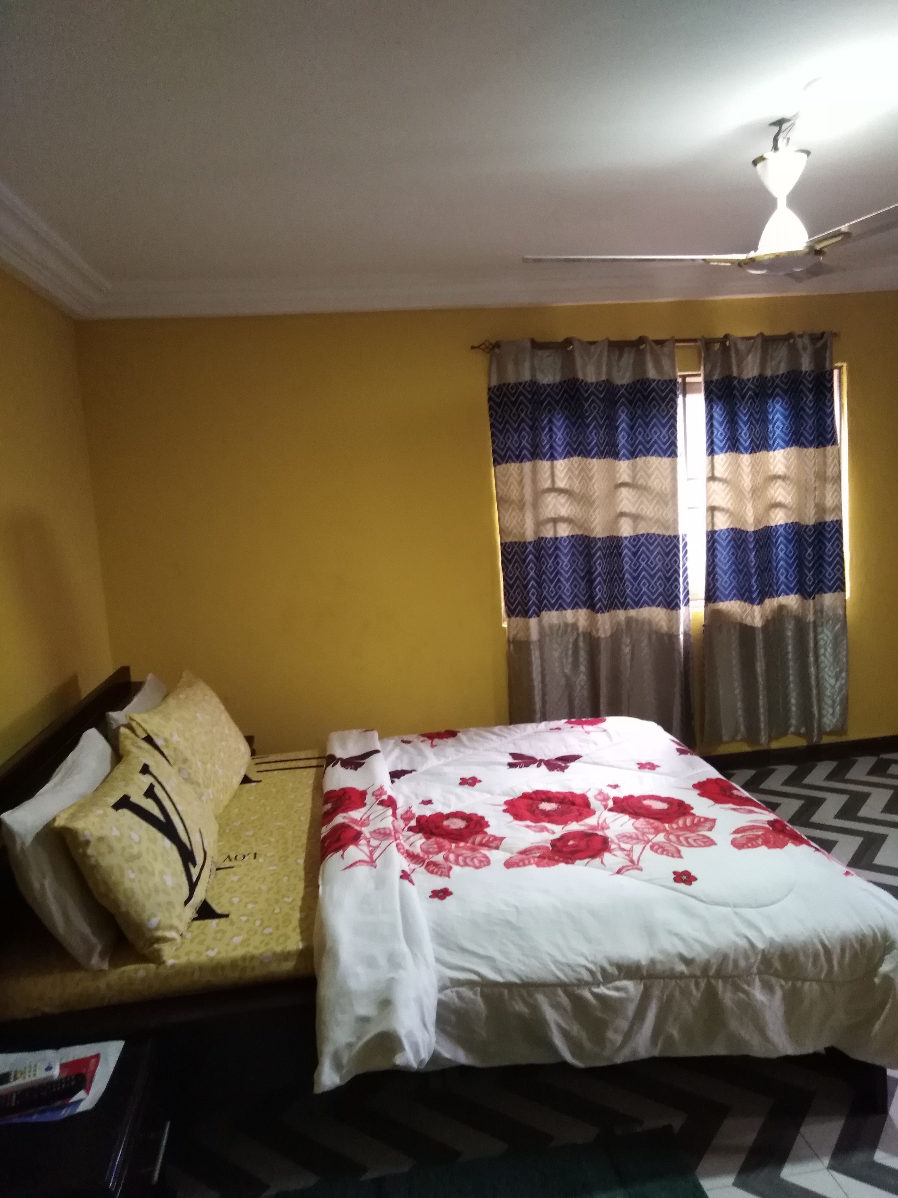 Quarto com cama, sofá, ventoinha no teto e cortinas.