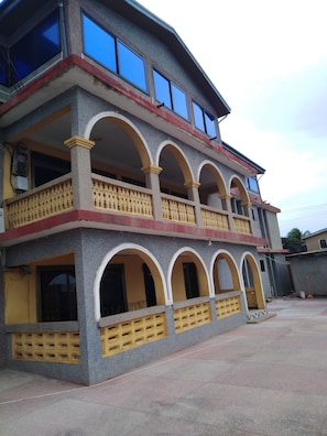 A multi-story building with a balcony on the upper floor, a covered entrance, and a gated entrance.