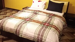 Una cama con colcha de cuadros, dos almohadas y una mesita de noche.