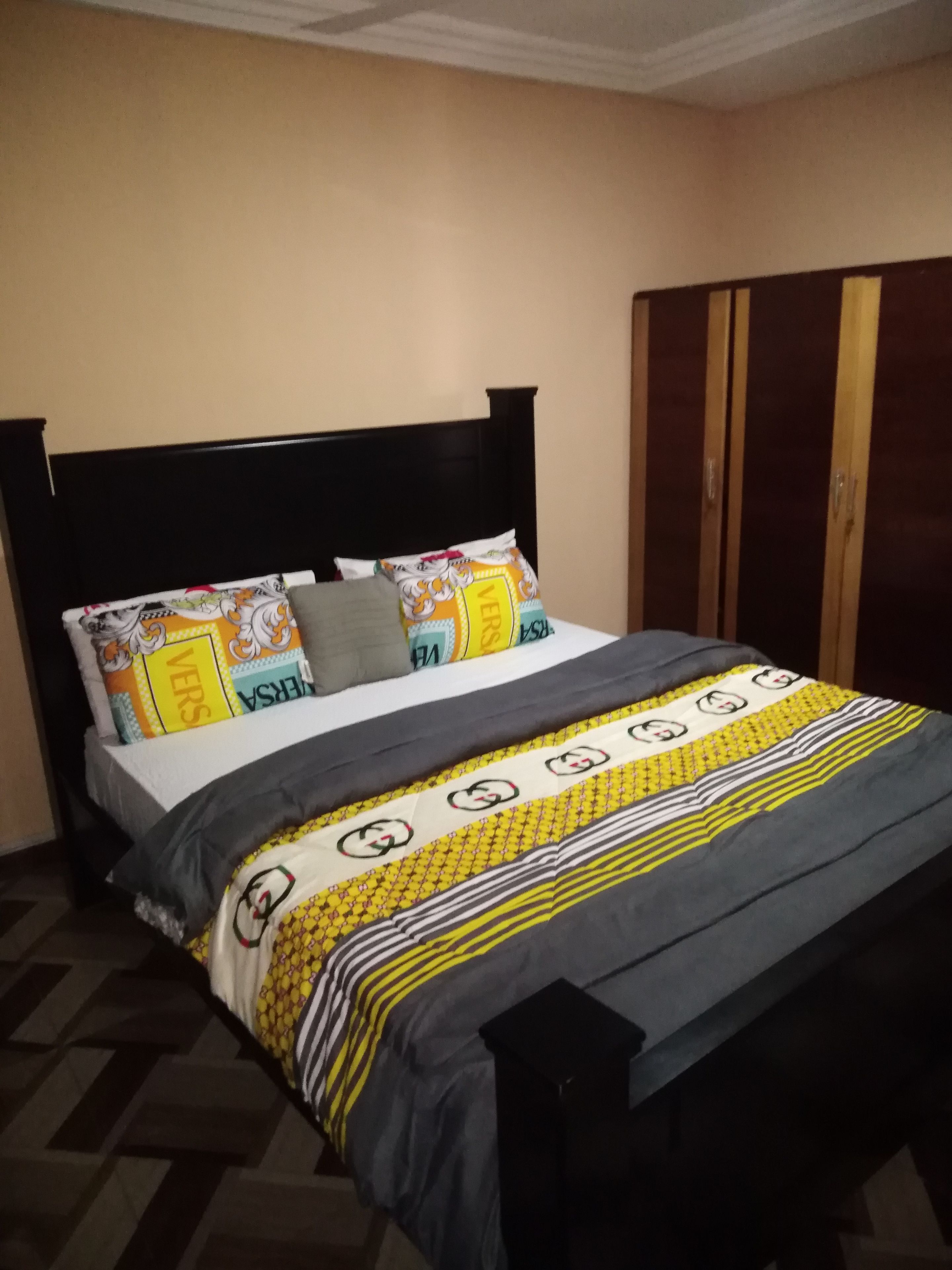Una cama con cabecera negra, colcha estampada y dos almohadas con diseño 'VERS'.