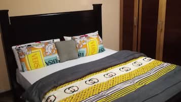 Una cama con cabecera negra, colcha estampada y dos almohadas con diseño 'VERS'.