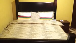 Una cama con cabecera oscura y colcha estampada, una mesita de noche con lámpara, y una pared con suelo de diseño geométrico.