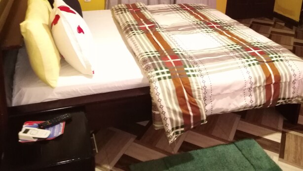 Una habitación con una cama, una mesita de noche, una puerta y un ventanal con cortinas.