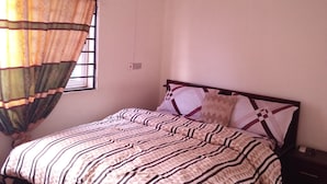 Un dormitorio con cama, ventilador de techo, aire acondicionado y una ventana con cortinas.