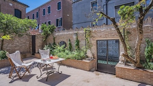 An outdoor patio with a table set for dining, surrounded by brick walls and potted plants. - STUNNING DORSODURO HOME WITH SECRET GARDEN & TWO PRIVATE TERRACES (Venezia)