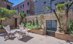 Une terrasse extérieure avec une table dressée pour le repas, entourée de murs en briques et de plantes en pot.
