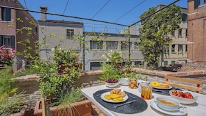 An outdoor dining area with a table set for a meal, surrounded by buildings and greenery. - STUNNING DORSODURO HOME WITH SECRET GARDEN & TWO PRIVATE TERRACES (Venezia)
